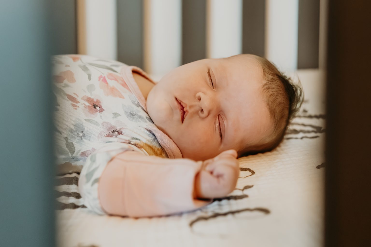 Newborn resting in her crib in a floral wrap
