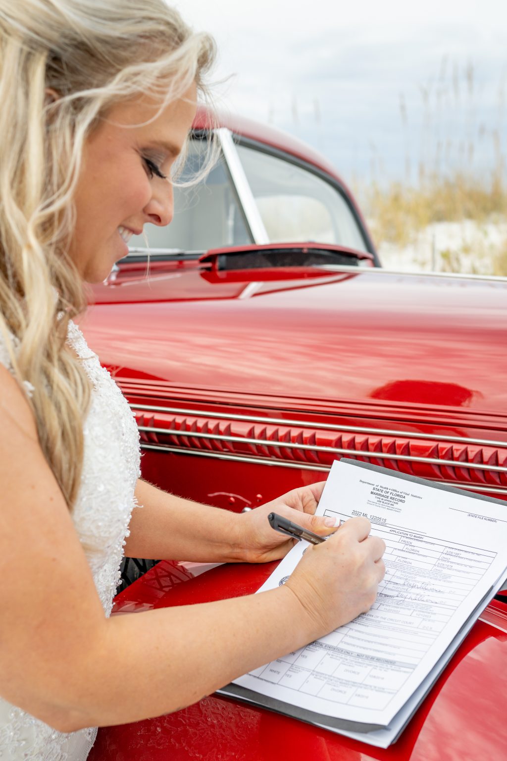 Bride signing the marriage license on a vintage red car