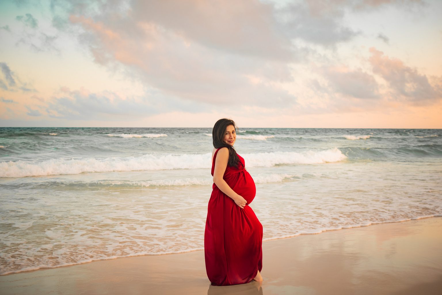Expectant mother in a flowing red gown at the shoreline