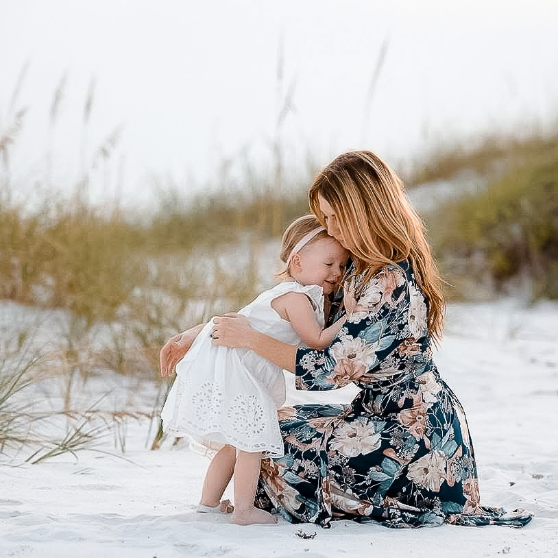 Amber Hubbard kneeling on the sand hugging her young daughter among the sea oats