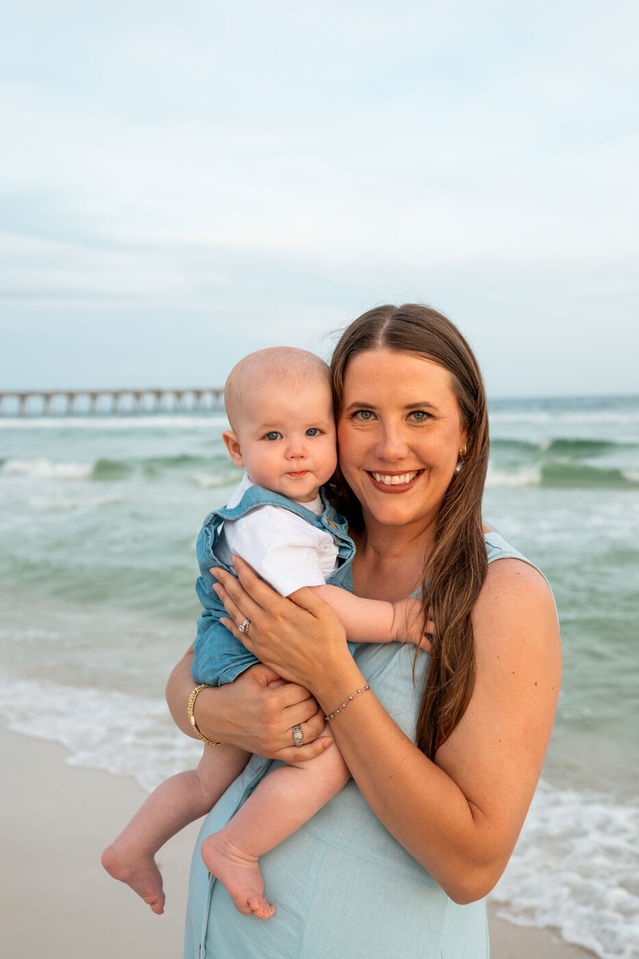 Mother in a blue dress holding her baby at the edge of the emerald Gulf water