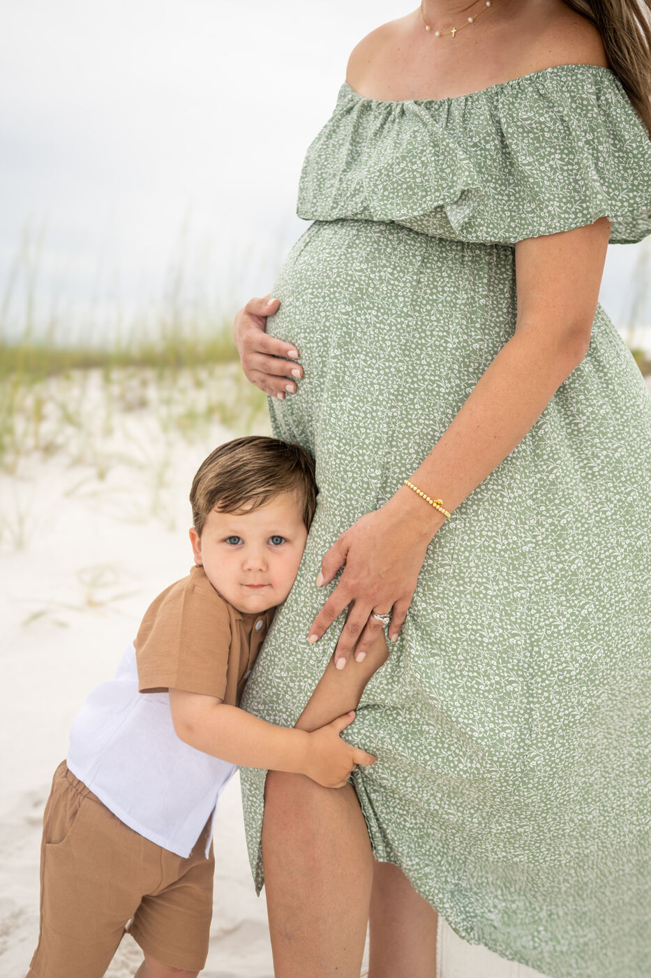 Toddler hugging his mother's baby bump during a beach maternity session