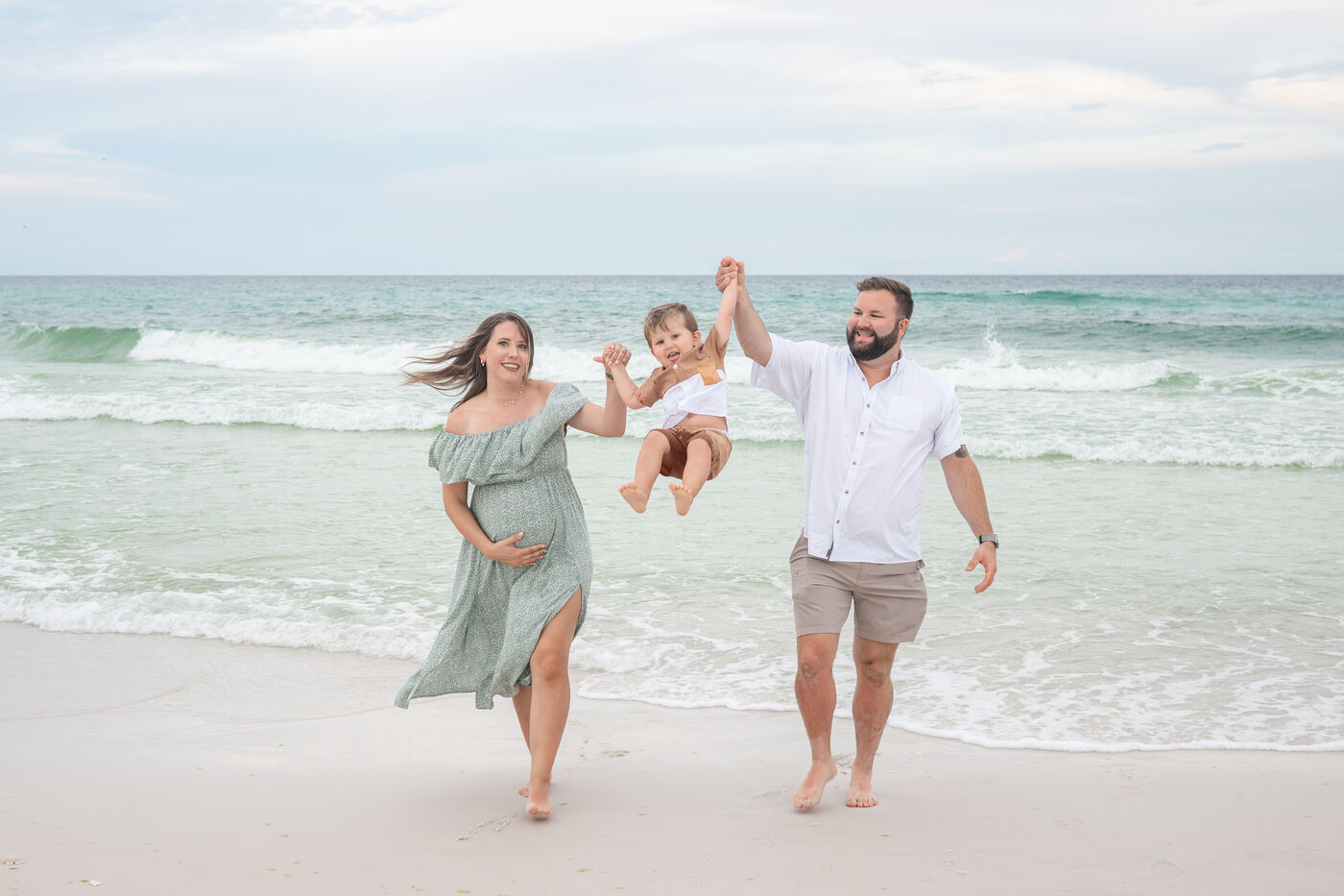 Expecting parents swinging their toddler at the water's edge