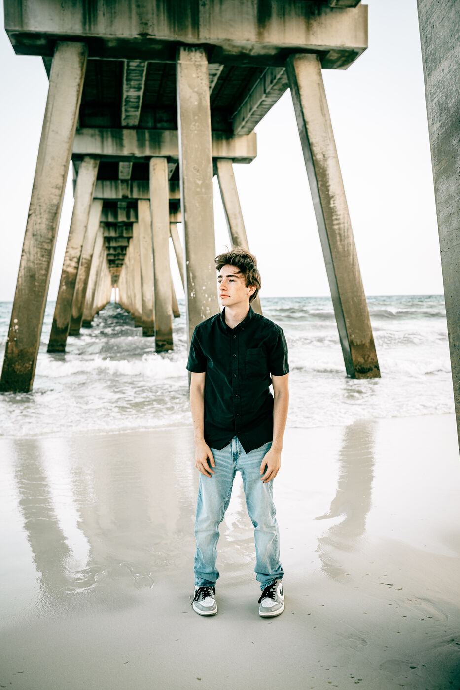 High school senior standing beneath the Navarre Beach pier at sunset